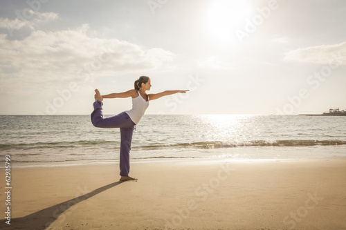 Young woman practicing dancer yoga pose near the ocean during su photo