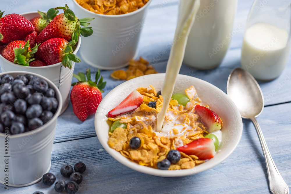 Pouring milk into cornflakes with fruits Pouring milk into cornflakes with fruits