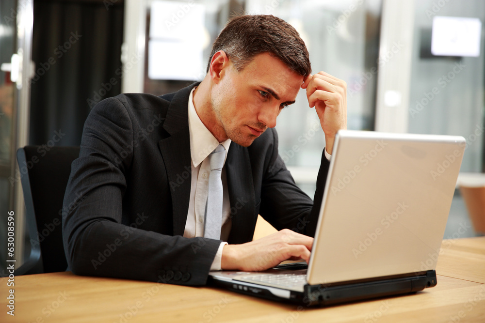 Confident businessman sitting with laptop at office Confident businessman sitting with laptop at office
