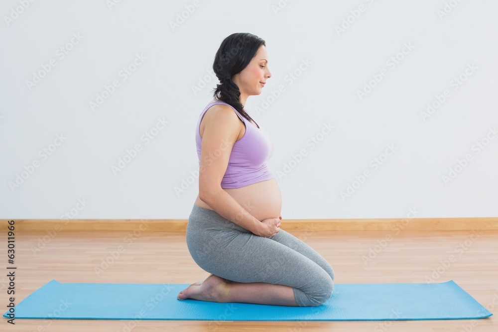 Pregnant brunette kneeling on exercise mat Pregnant brunette kneeling on exercise mat