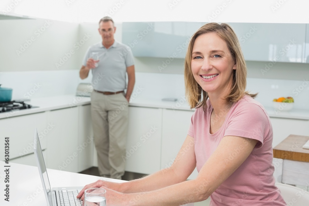 Fototapeta premium Woman using laptop while man drinking water in kitchen