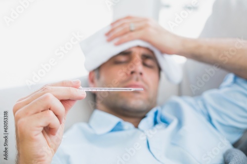 Sick man lying on sofa checking his temperature photo