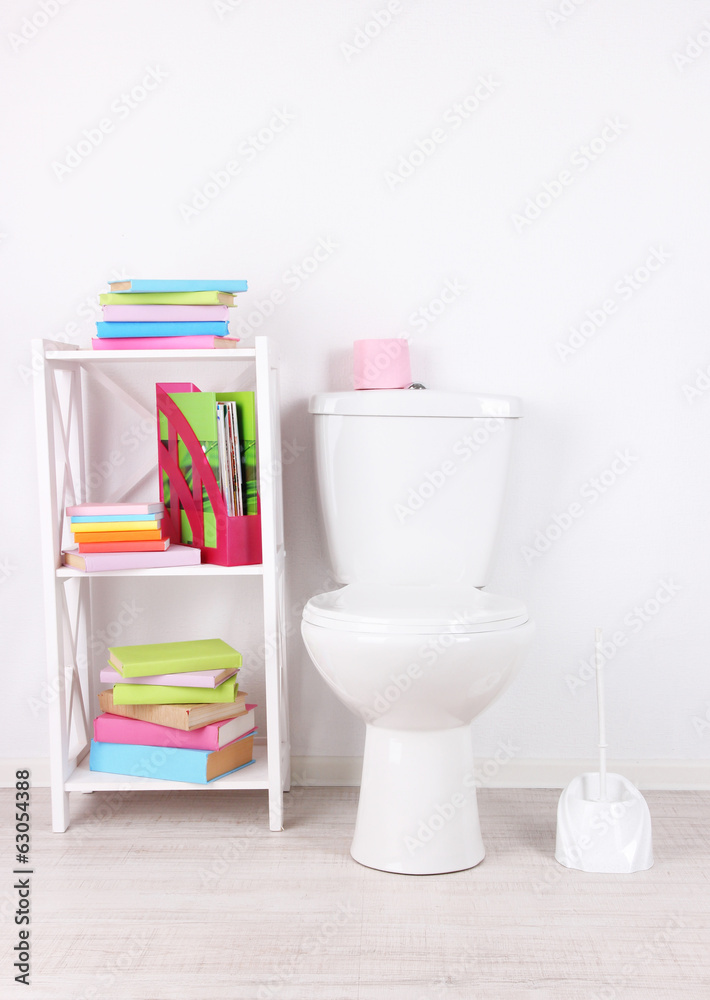 White toilet bowl and stand with books, on color wall White toilet bowl and stand with books, on color wall
