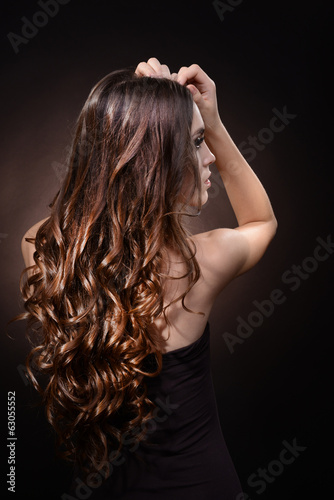 Beautiful young woman with long hair on dark brown background