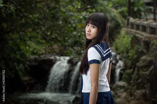 Asian schoolgirl standing in front of waterfall