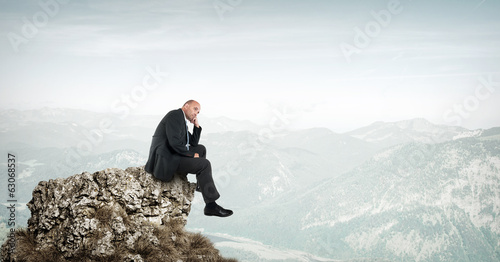 Businessman sitting on a rock in the mountains photo