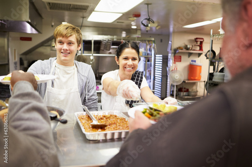 Staff Serving Food In Homeless Shelter Kitchen
