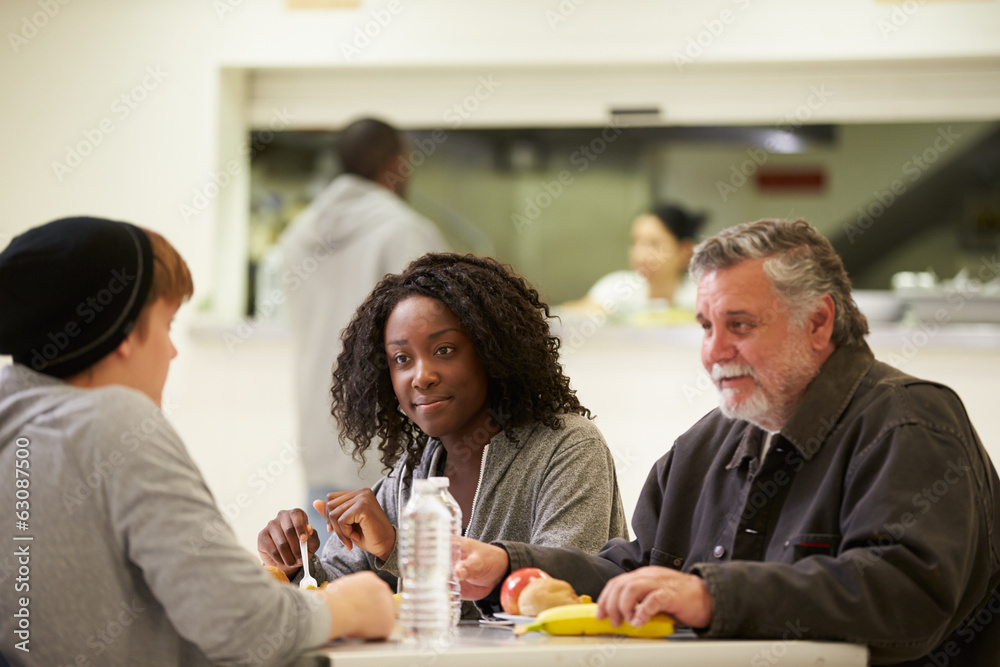 People Sitting At Table Eating Food In Homeless Shelter People Sitting At Table Eating Food In Homeless Shelter