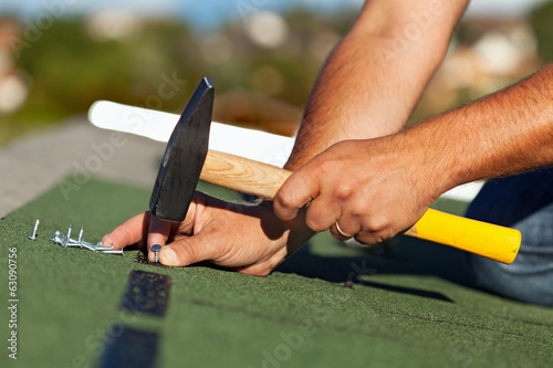 Man hands fastening bitumen roof shingles