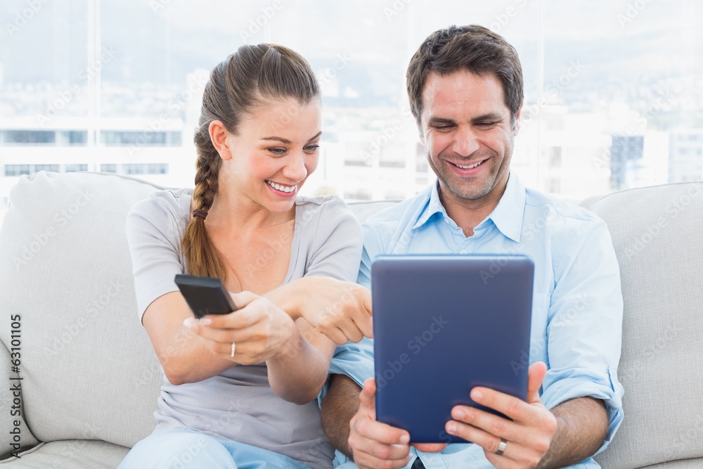 Happy couple sitting on the couch using tablet pc and watching t Happy couple sitting on the couch using tablet pc and watching t