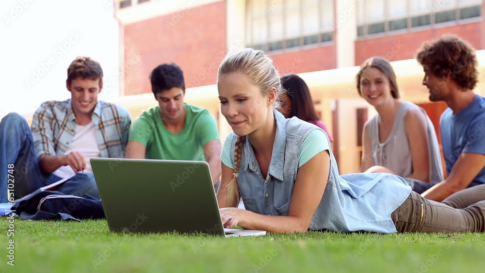 Blonde student using laptop with classmates sitting behind Blonde student using laptop with classmates sitting behind