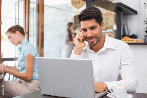 Man using laptop and mobile phone in coffee shop