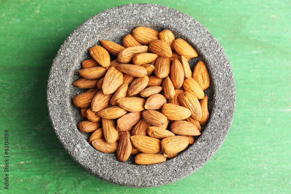 Almonds in bowl on color wooden background