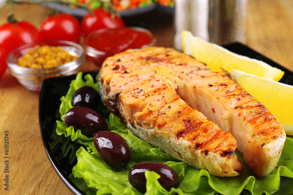 Tasty grilled salmon with lemon and vegetables, on wooden table Tasty grilled salmon with lemon and vegetables, on wooden table