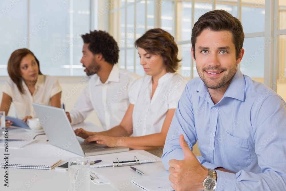 Smiling businessman gesturing thumbs up with colleagues in meeti Smiling businessman gesturing thumbs up with colleagues in meeti