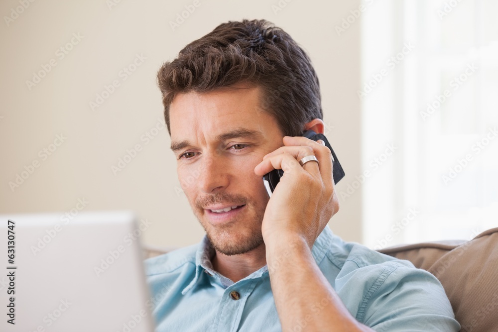 Smiling man using laptop and mobile phone in living room Smiling man using laptop and mobile phone in living room