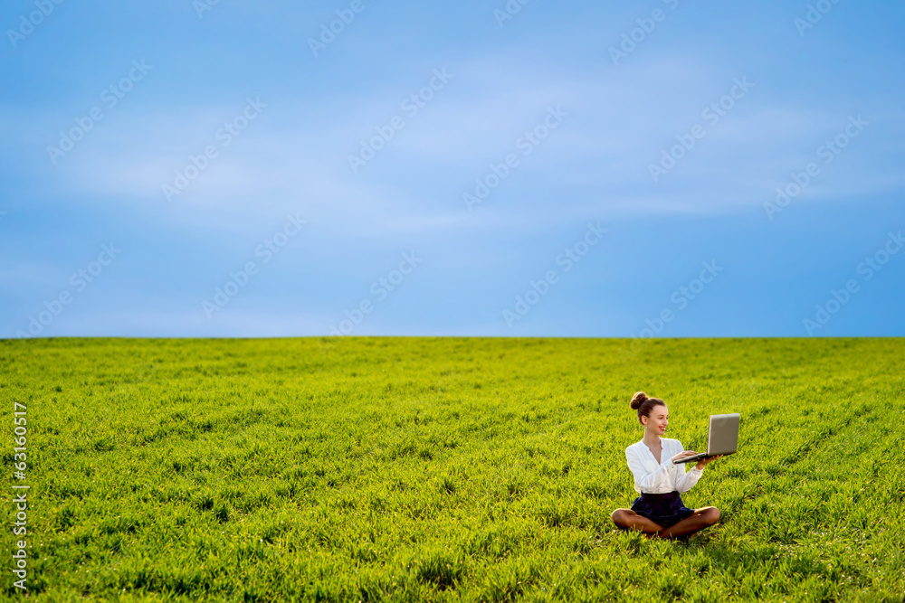 Young woman, girl working with laptop in green field with blue s Young woman, girl working with laptop in green field with blue s