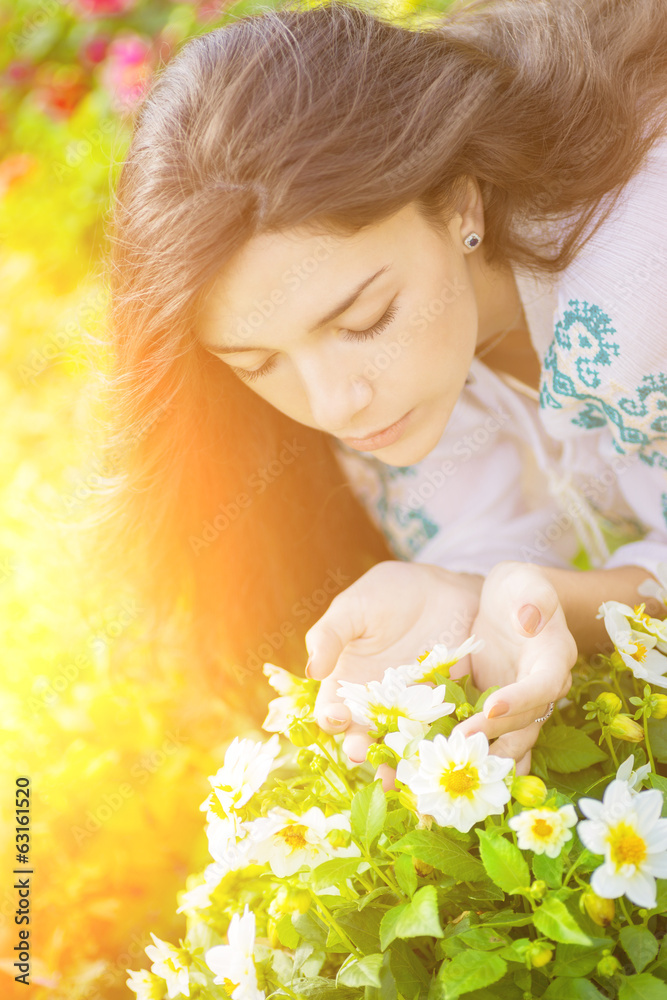 Fototapeta premium Young girl smelling flowers in garden with the sunshine.