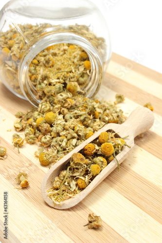 Dried chamomile in glass jar and on wooden spoon