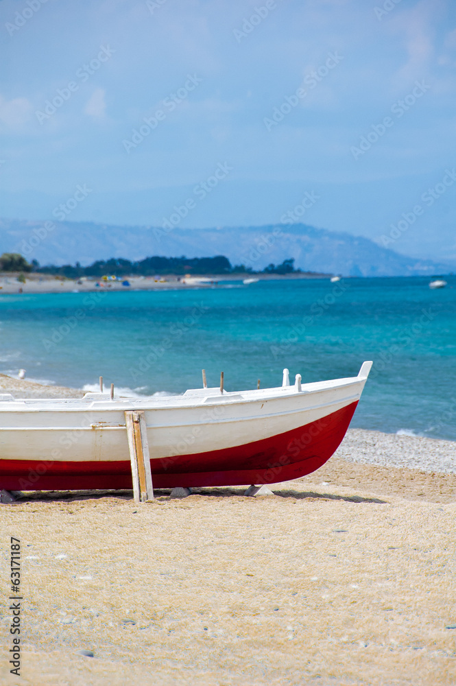A red and white wooden boat on a beach in the south of Italy