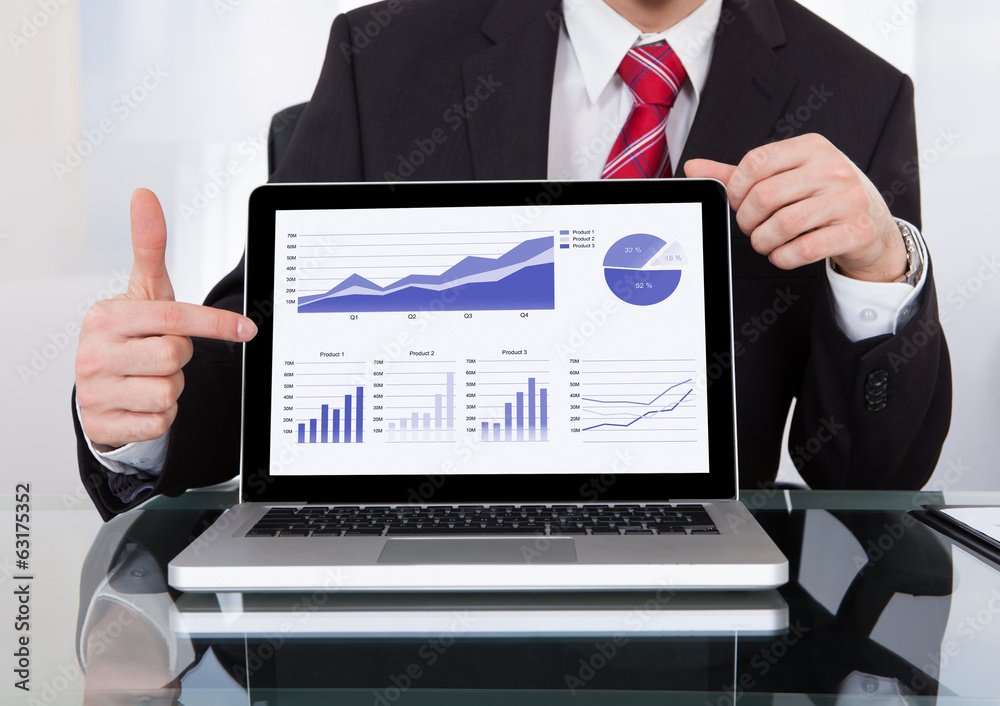Confident Businessman Displaying Laptop At Desk Confident Businessman Displaying Laptop At Desk