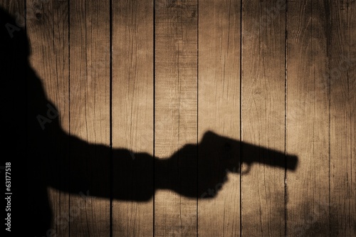 Outstretched arm with a gun. Black shadow on wooden background. photo