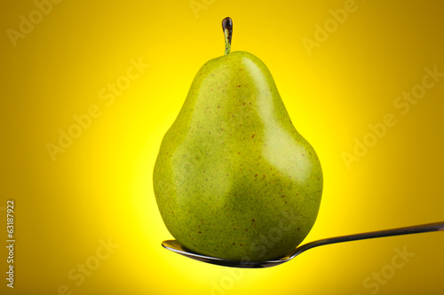 Green pear in silver spoon on yellow background