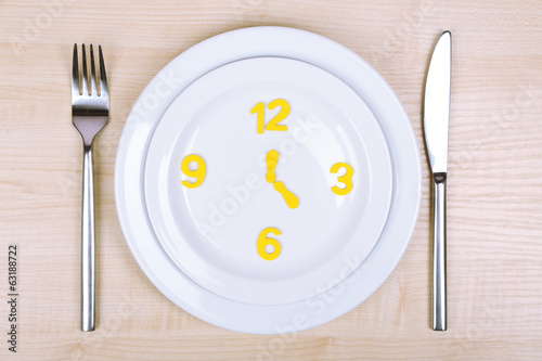 Plate with clock on wooden table close-up