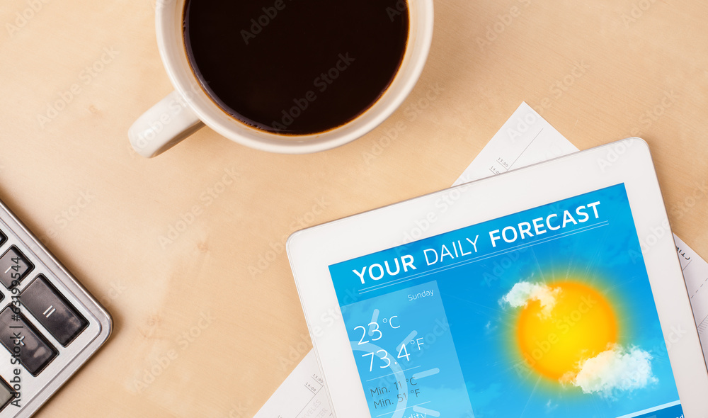 Tablet pc showing weather forecast on screen with a cup of coffe Tablet pc showing weather forecast on screen with a cup of coffe