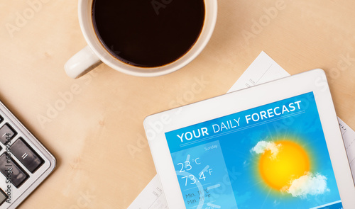 Tablet pc showing weather forecast on screen with a cup of coffe