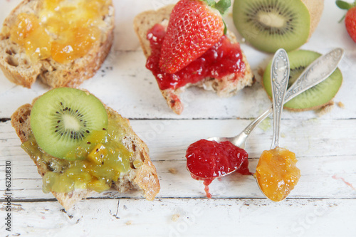 kiwi, orange and strwberry jam with slices of bread on wooden ta photo