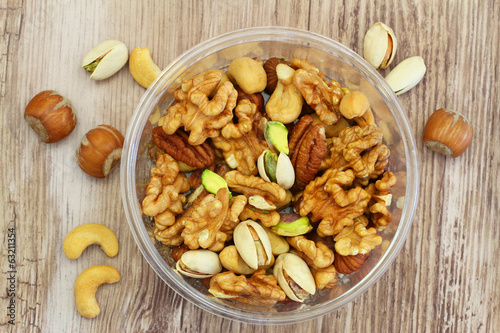 Selection of mixed nuts in plastic box on wooden surface