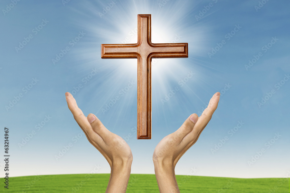 Male hands praying with a wooden cross