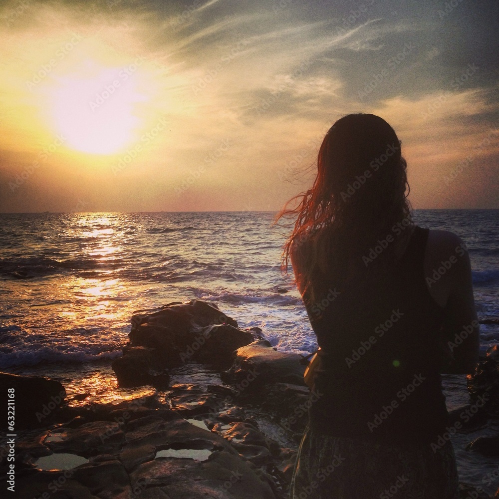 girl looks out to sea at sunset 