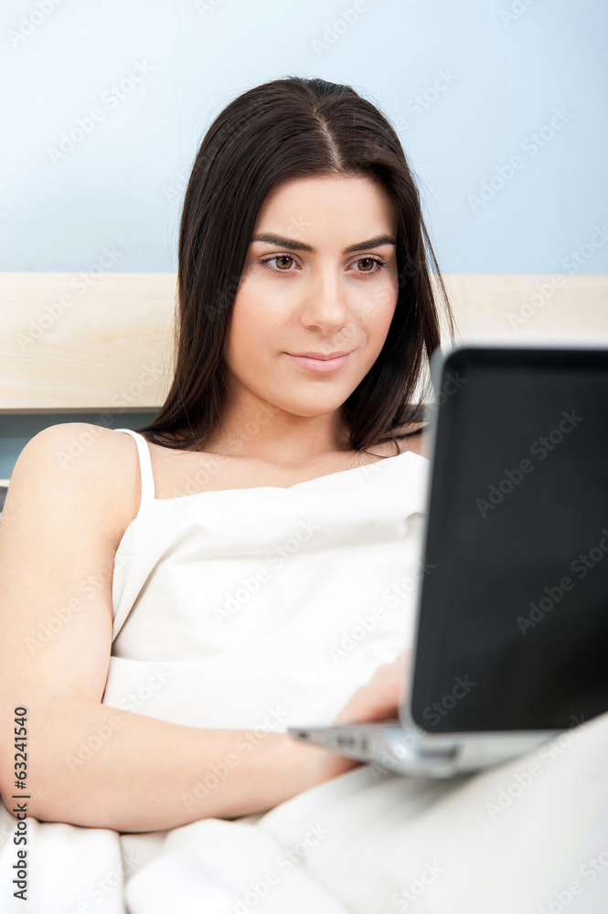 Beautiful woman relaxing on her bed working with her laptop Beautiful woman relaxing on her bed working with her laptop