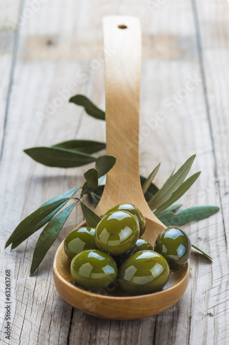 Cuchara de palo con olivas verdes sobre fondo de madera