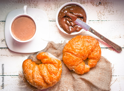 Fresh baked croissants with chocolate cream and hot cocoa on woo