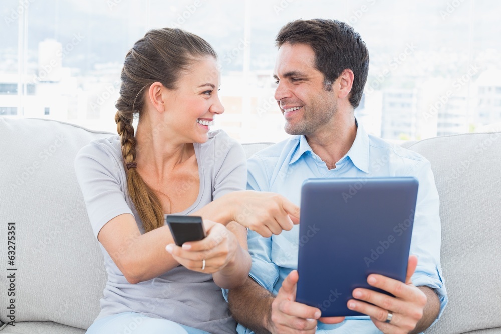 Smiling couple sitting on the couch using tablet pc and watching Smiling couple sitting on the couch using tablet pc and watching