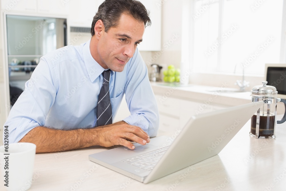 Concentrated well dressed man using laptop in kitchen Concentrated well dressed man using laptop in kitchen
