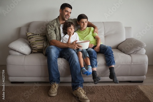 Father and sons with popcorn bowl watching tv in the living room