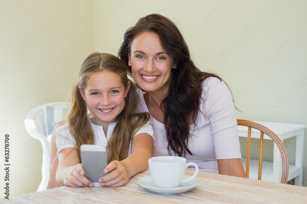 Woman and daughter holding mobile phone at table Woman and daughter holding mobile phone at table