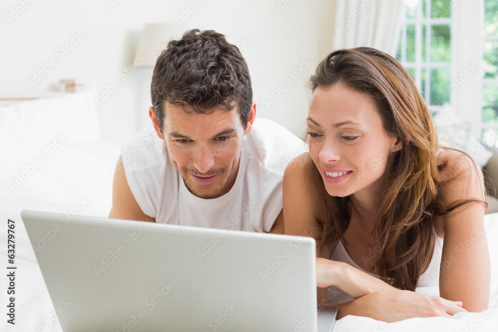 Smiling couple using laptop in bed Smiling couple using laptop in bed