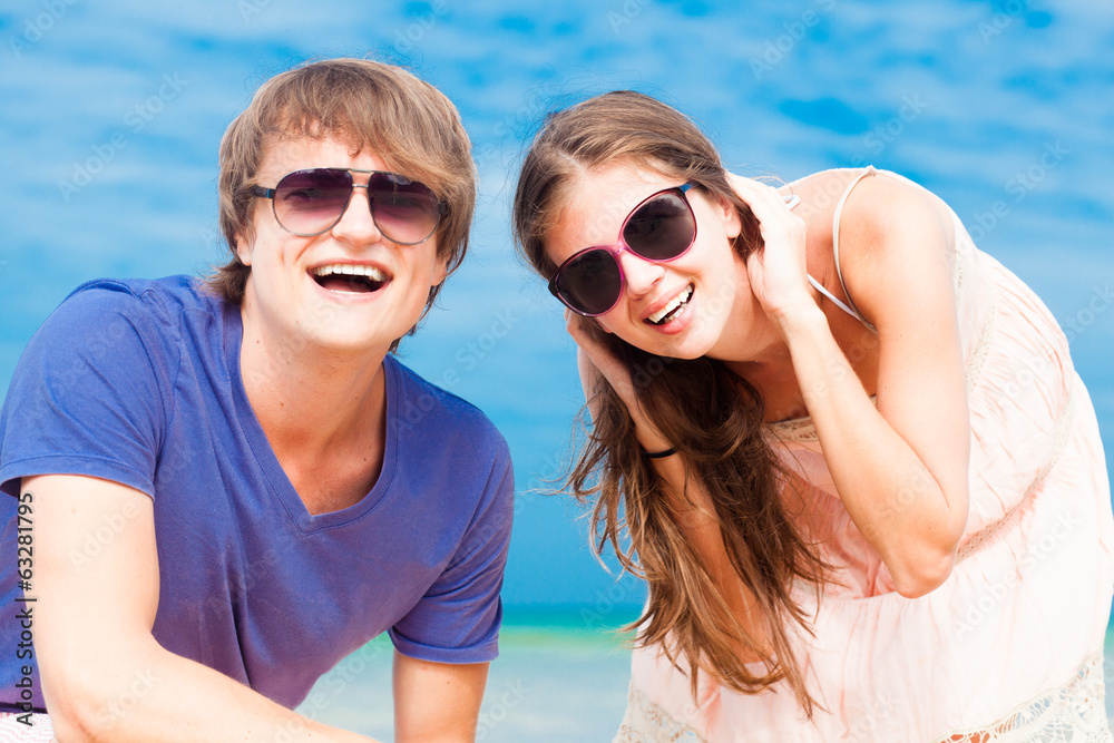Closeup of happy young couple in sunglasses on beach smiling and