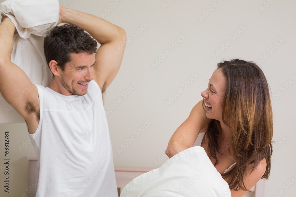 Cheerful couple pillow fighting in bed Cheerful couple pillow fighting in bed