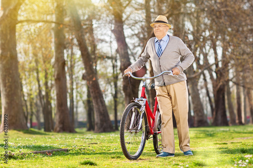An elderly pushing his bike in the park