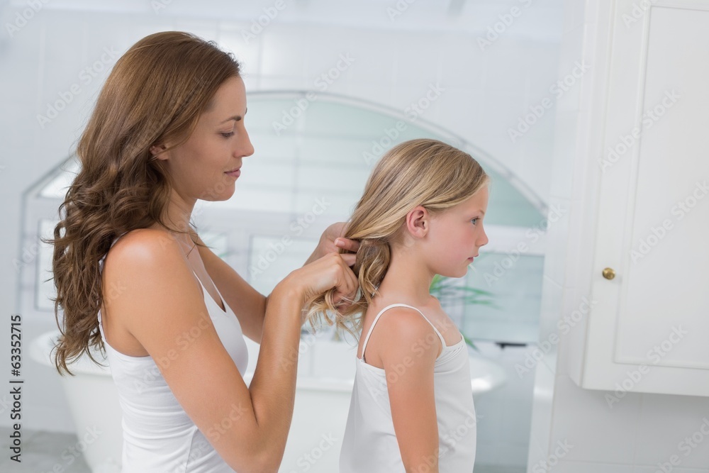 Woman braiding cute little girl's hair in bathroom Woman braiding cute little girl's hair in bathroom