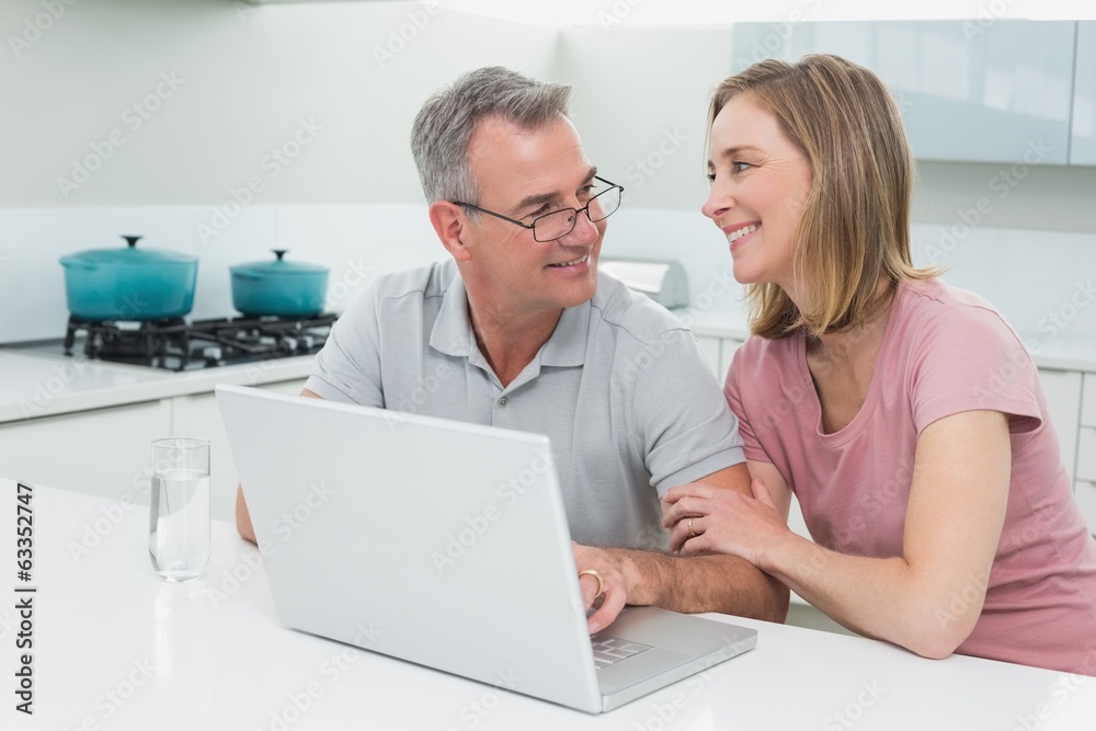 Obraz premium Smiling couple using laptop in kitchen