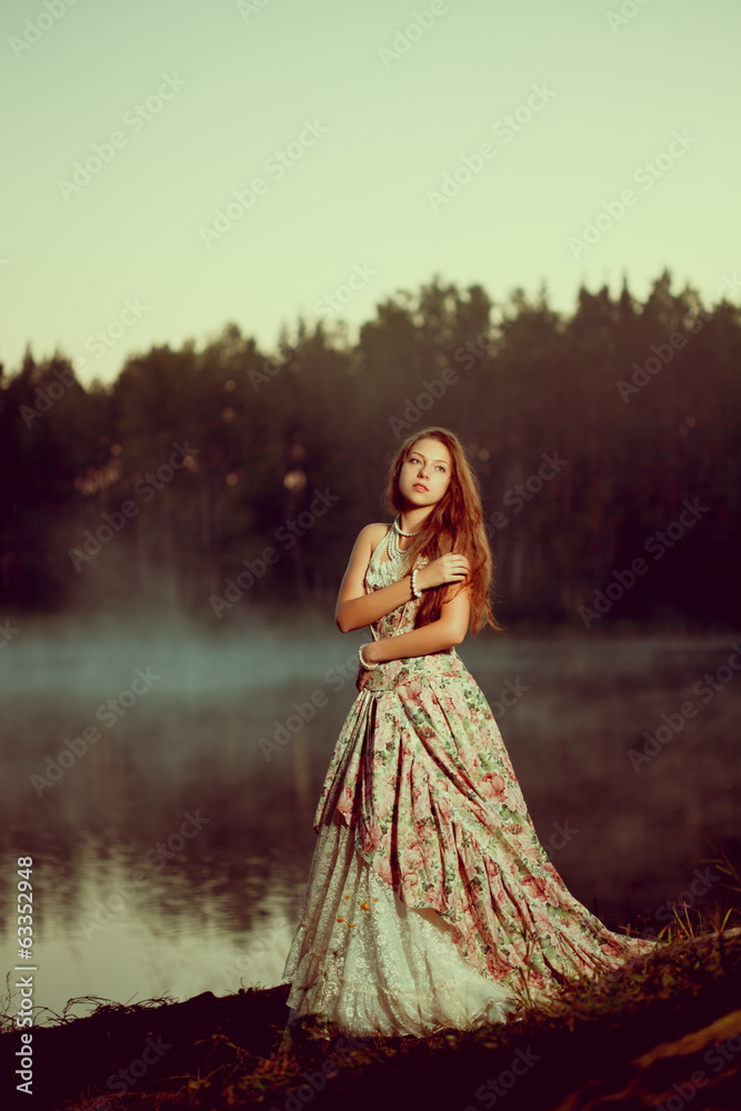 Luxury woman in a forest in a long vintage dress near the lake.