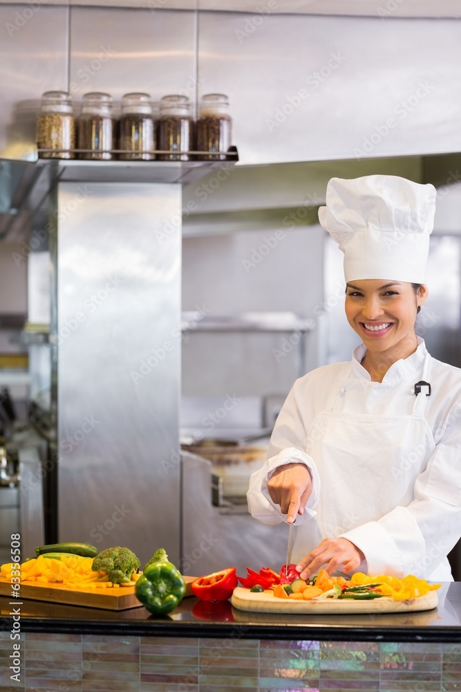 Smiling female chef cutting vegetables in kitchen