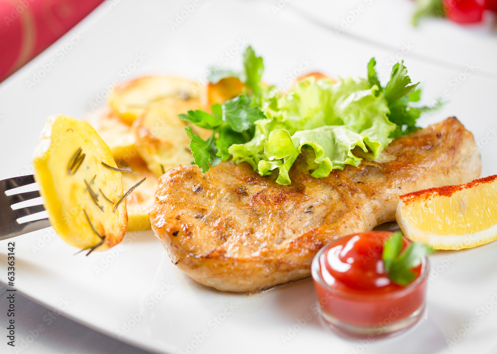 Roasted pork chop with potatoes, ketchup and lemon on dish Roasted pork chop with potatoes, ketchup and lemon on dish